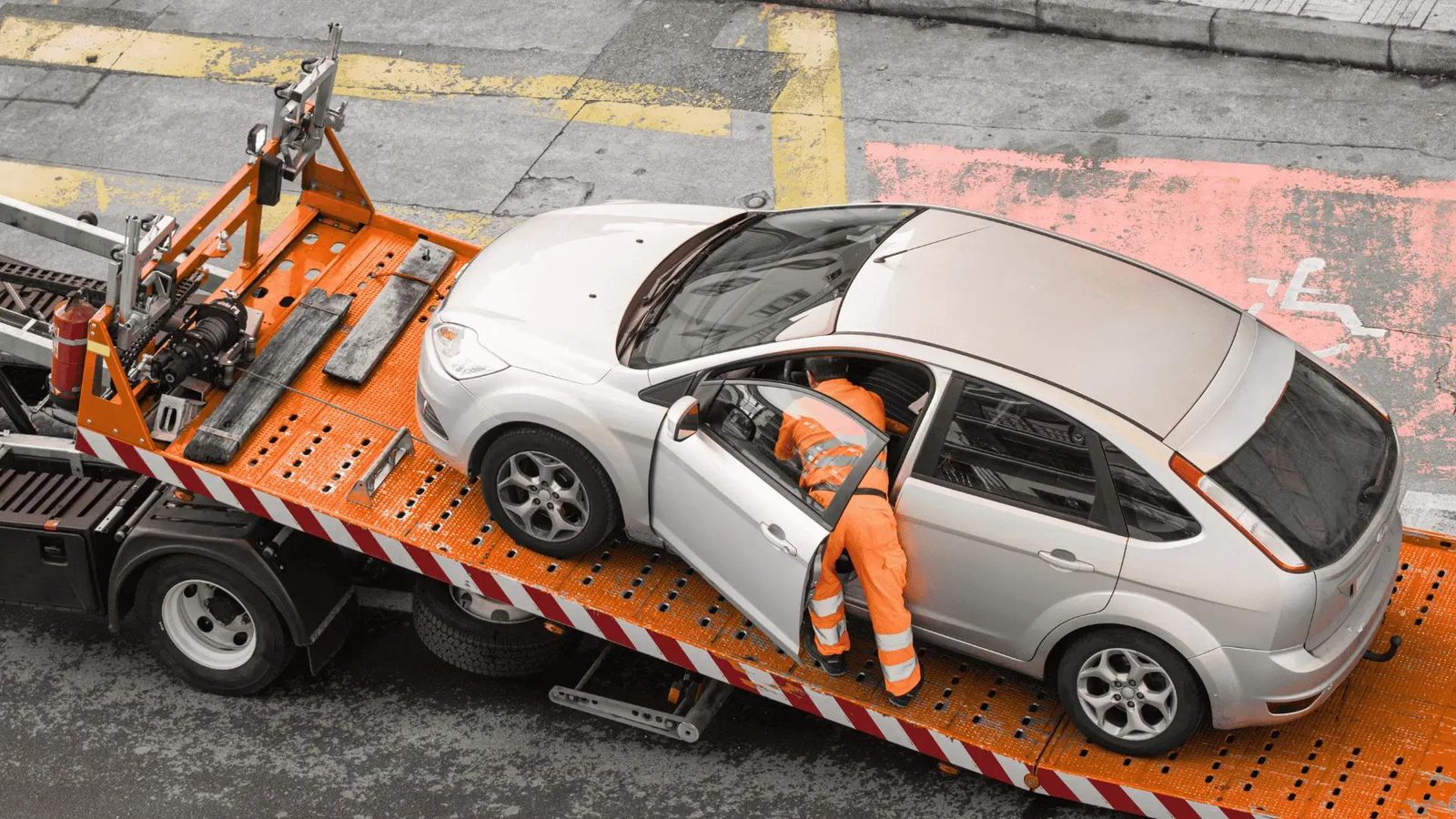 Car loaded on an orange flatbed tow truck, seen from above