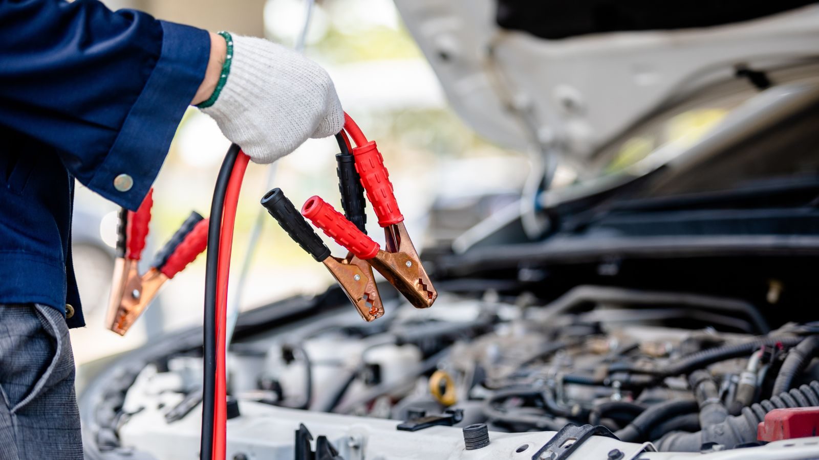 Driver holding jumper cable clamps over an open car engine bay